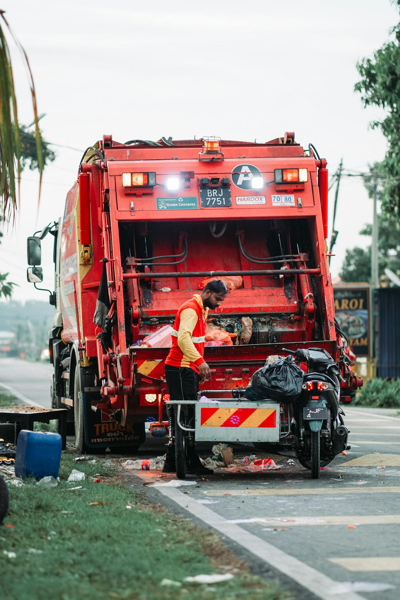 A sanitation worker managing waste disposal behind a garbage truck in Klang, Selangor.