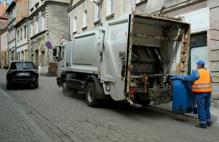 City street scene with garbage truck and worker handling waste bin.