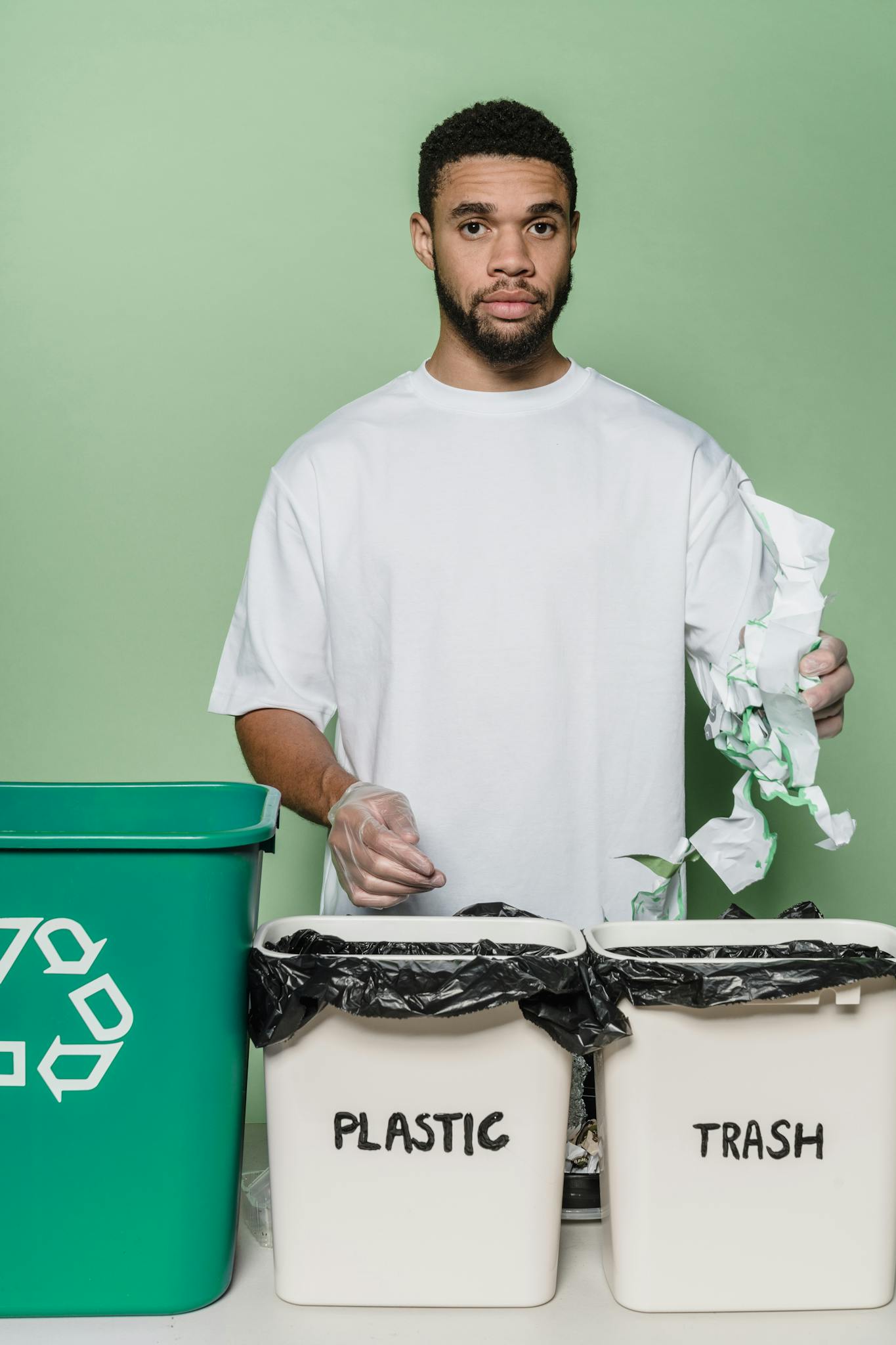 Man recycling plastic and trash in a studio with green background. Promotes eco-awareness and sustainability.