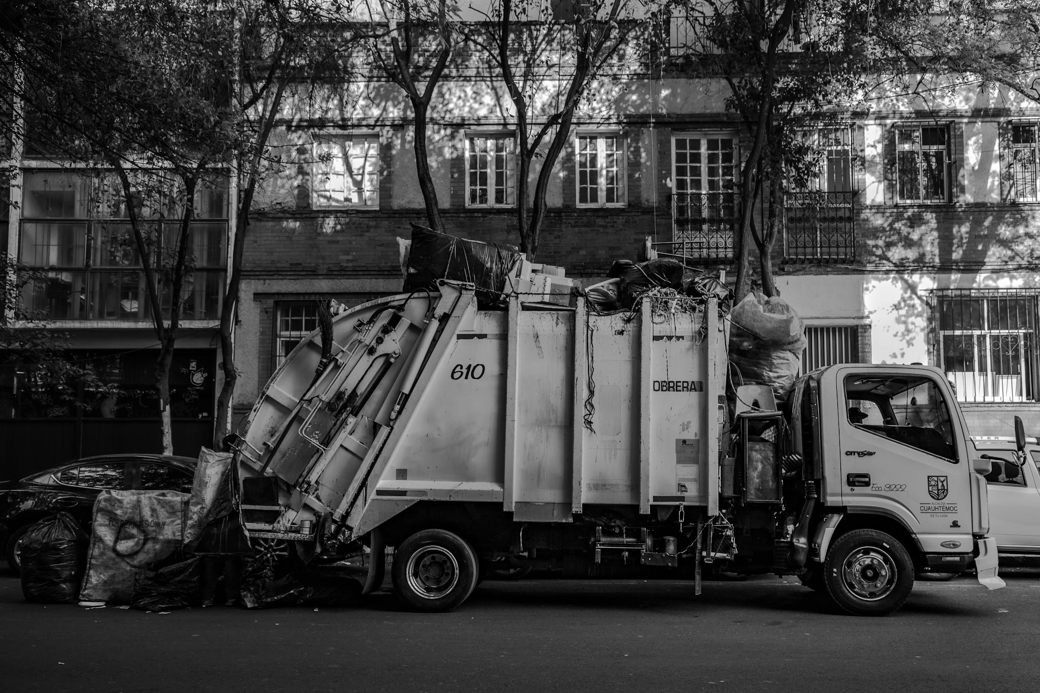 Monochrome photo of a garbage truck collecting trash in an urban area.