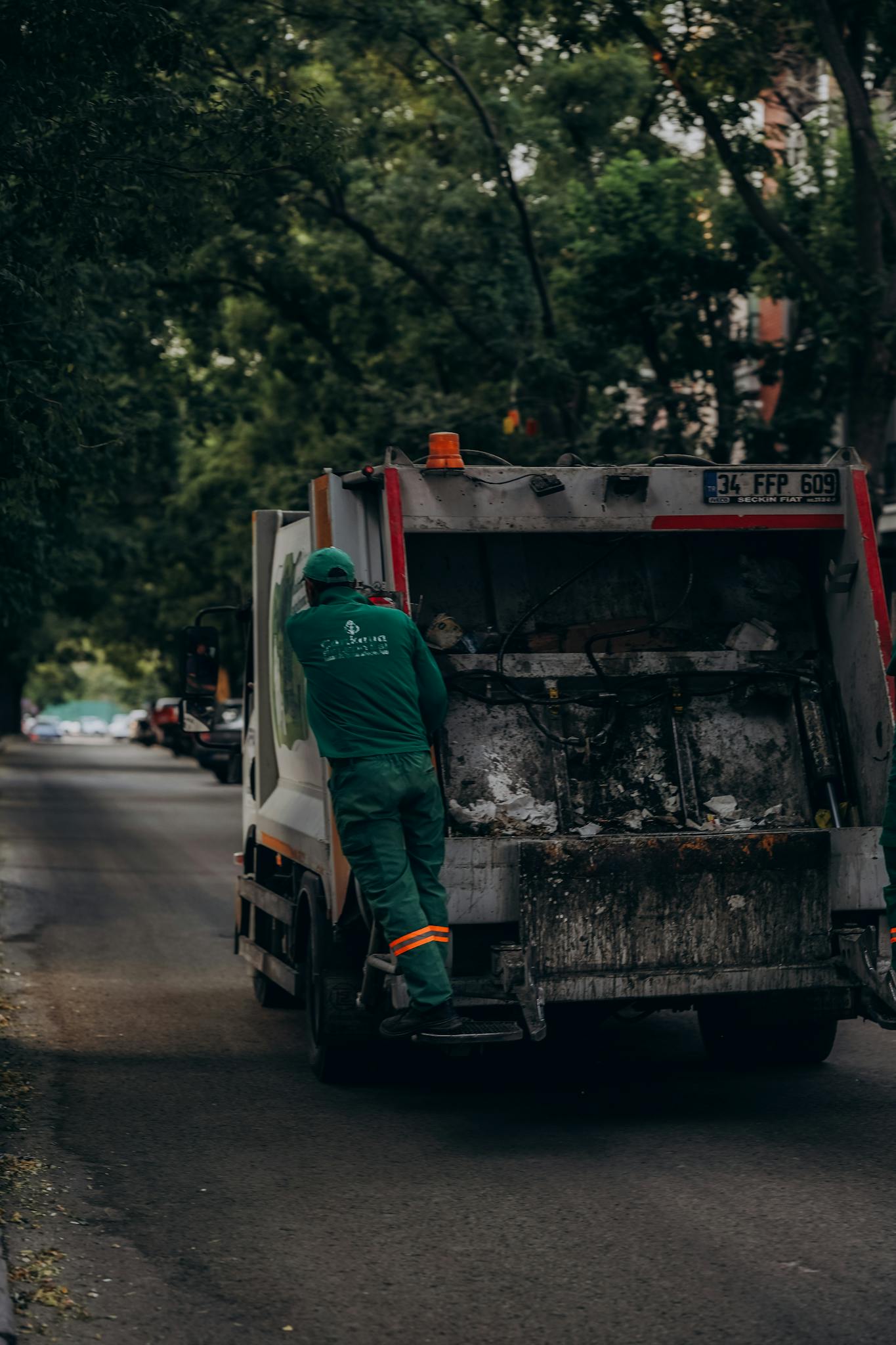 Sanitation worker on a garbage truck in a tree-lined street of Ankara, Türkiye.